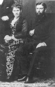 Black and white image of Franklin sitting near a woman in a floral dress. 
