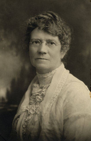 Black and white headshot of Ruth wearing a white blouse and glasses