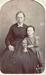 Woman seated with small daughter standing beside her.